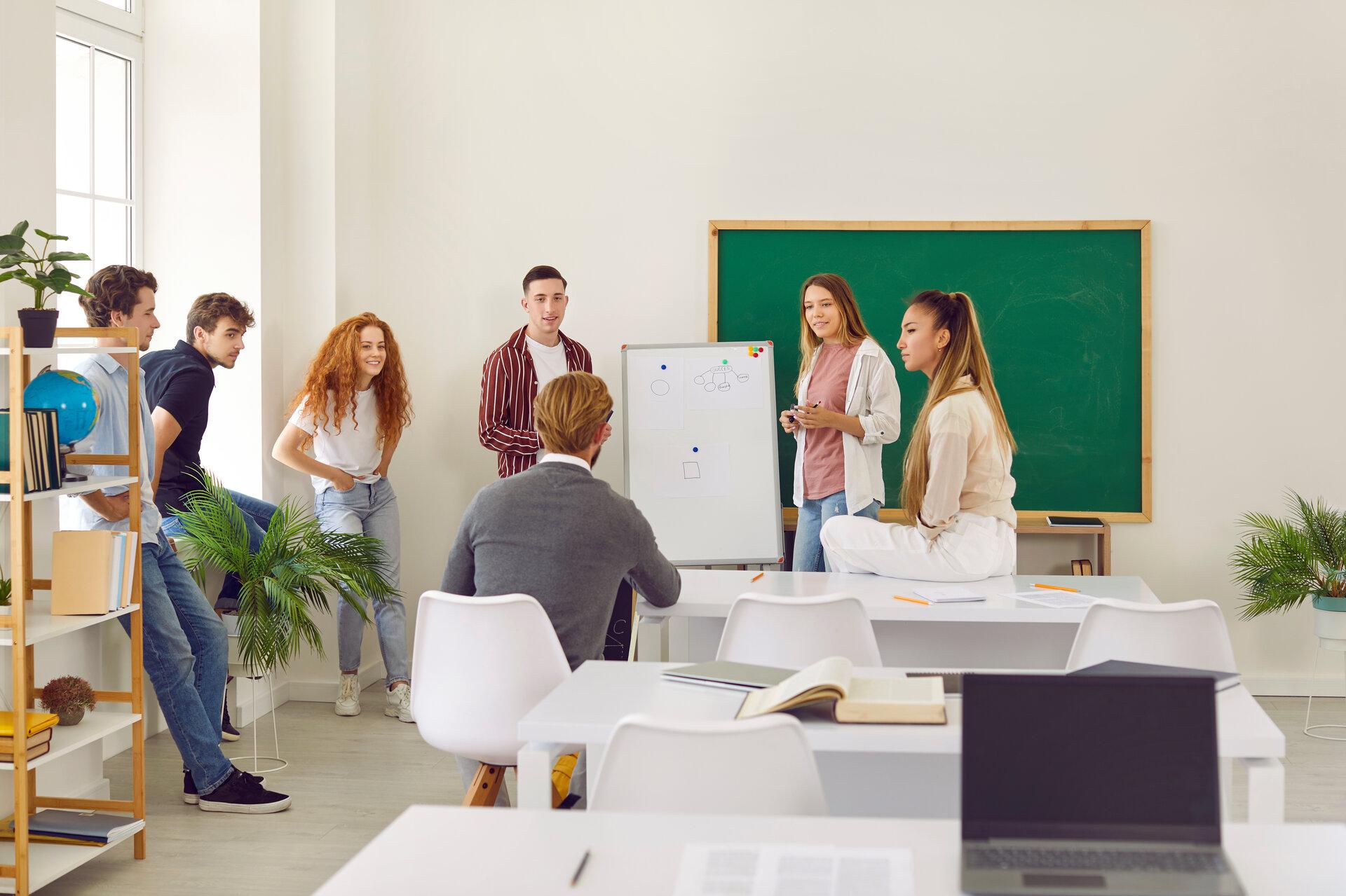 Eine Gruppe von Schülern, Studenten oder Hochschulstudenten, die in einem geräumigen Klassenzimmer Unterricht haben, dem Lehrer zuhören, neue Themen diskutieren, Präsentationen machen und gemeinsam Neues lernen.